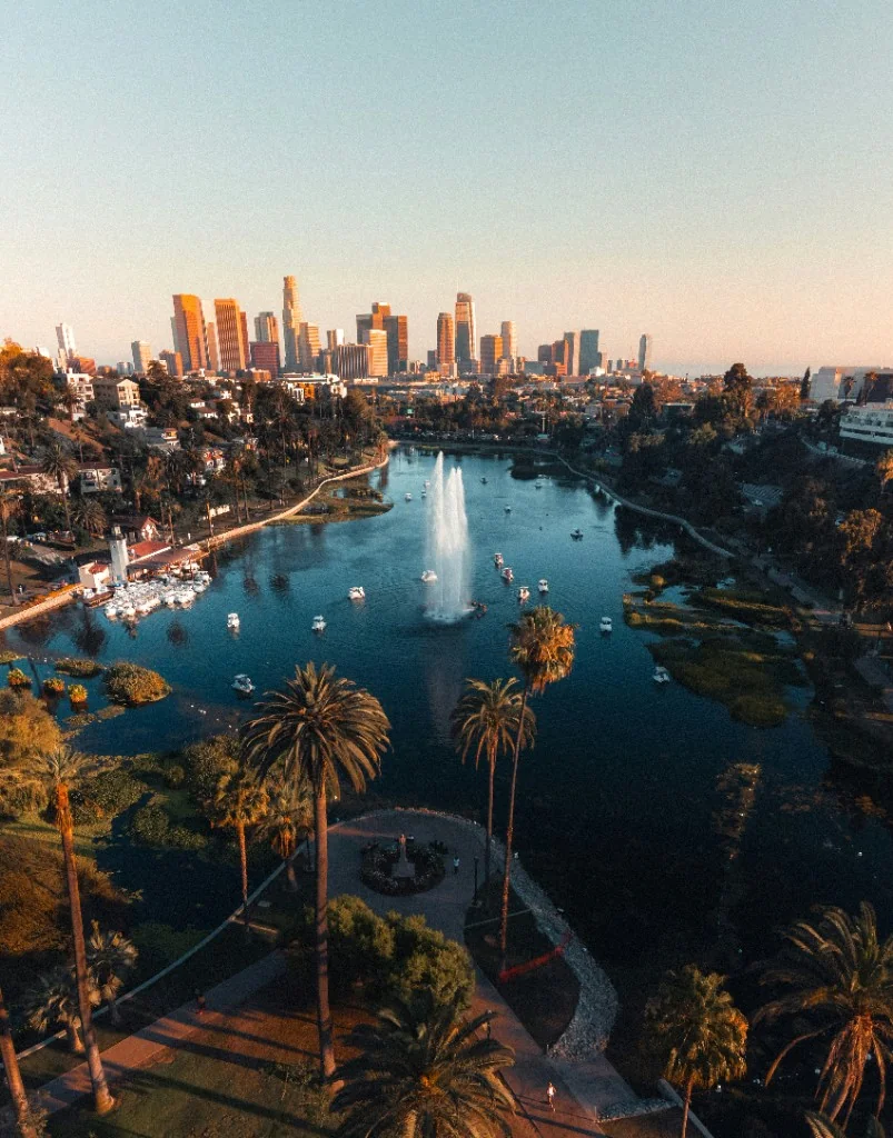 Aerial view of a lake with a fountain, palm trees, and a distant skyline.